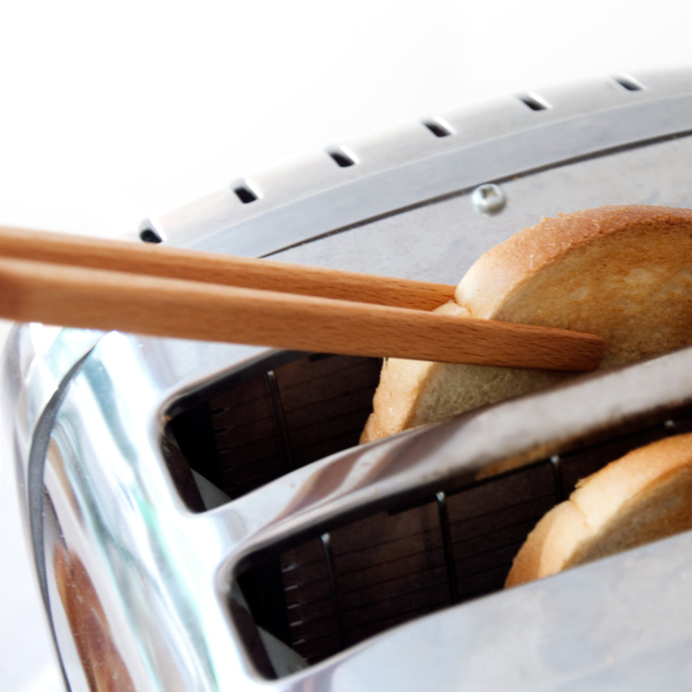 Toastzange greift nach Toastscheibe in Toaster Buchenholz